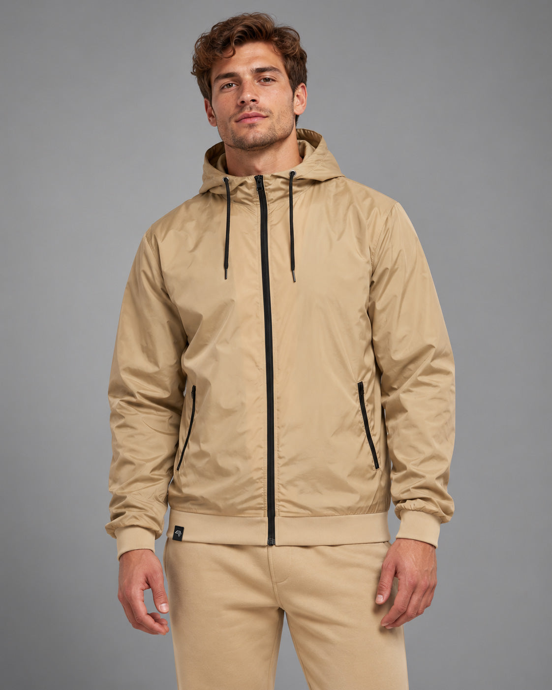 Windjacke BBD 6100 in Beige / Black an Herrenmodel im Studio – sandbeiger Nylon-Blouson mit schwarzem Frontreißverschluss, Kapuze mit Kordelzug, seitlichen Zip-Taschen und breiten Rippbündchen