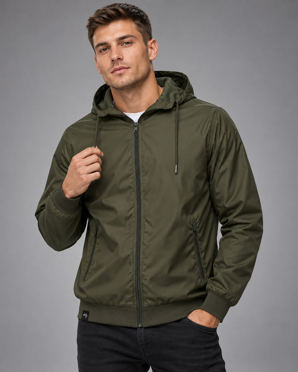 BBD 6100 Nylon-Windjacke am männlichen Model, Olive-farbene Kapuzenjacke mit gleichfarbigen Reißverschlüssen, Kordeln, zwei schrägen Zip-Taschen und sportlichem Rippbund