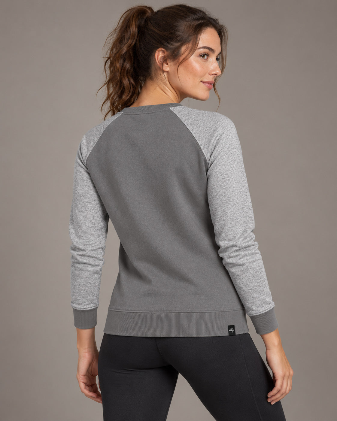 Grau Solid / Melange – zweifarbiges Damen-Raglansweatshirt am Model in Dreiviertel-Rückenansicht, mit hellgrau melierten Ärmeln, diagonalen Rückennähten und breitem Rippbund.